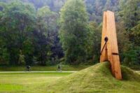 Übergroße hölzerne Wäscheklammer, die in einem Park ein Stück Wiese aufwirft und einklemmt. Möglicherweise eine Kunst-Skulptur