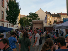 Totale über das Straßenfest. Im Vordergrund etliche Besucher von hinten, im Hintergrund vor den Besuchern die Bühne mit Hazard Dawn